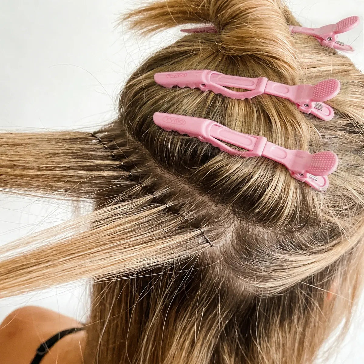 Back view of a person sectioning blonde hair into precise layers using pink TYMO Alligator Sectioning Clips during heat styling