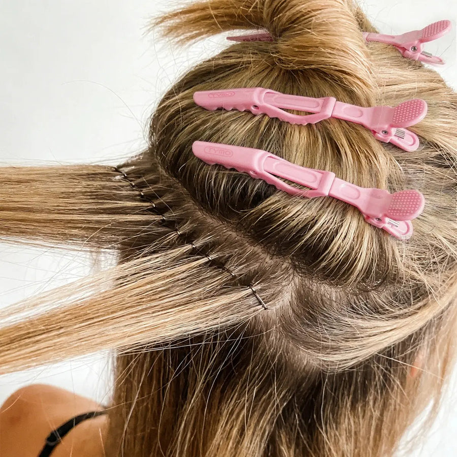 Back view of a person sectioning blonde hair into precise layers using pink TYMO Alligator Sectioning Clips during heat styling