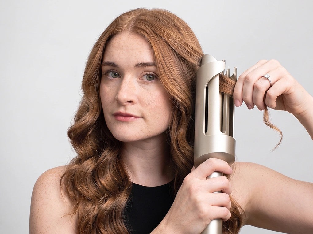 Woman using the TYMO CURLPRO PLUS automatic hair curler to create soft, defined curls in her long auburn hair.